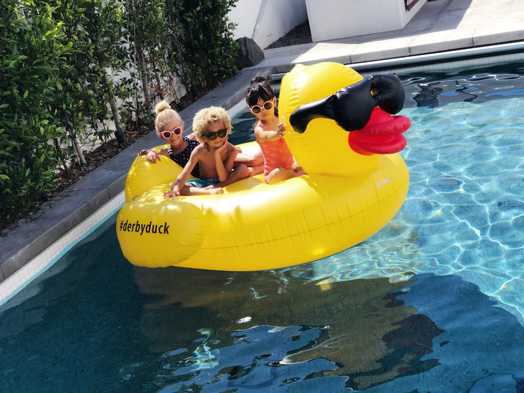 Three children on a yellow inflatable duck float in a pool.
