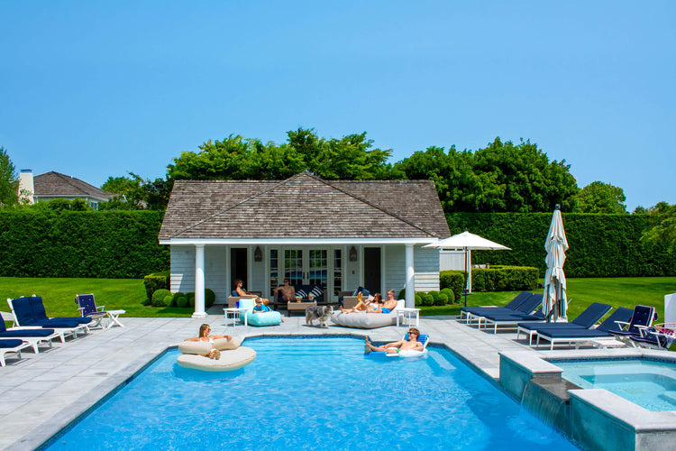 People relaxing by a pool with a small building and lounge chairs in the background.