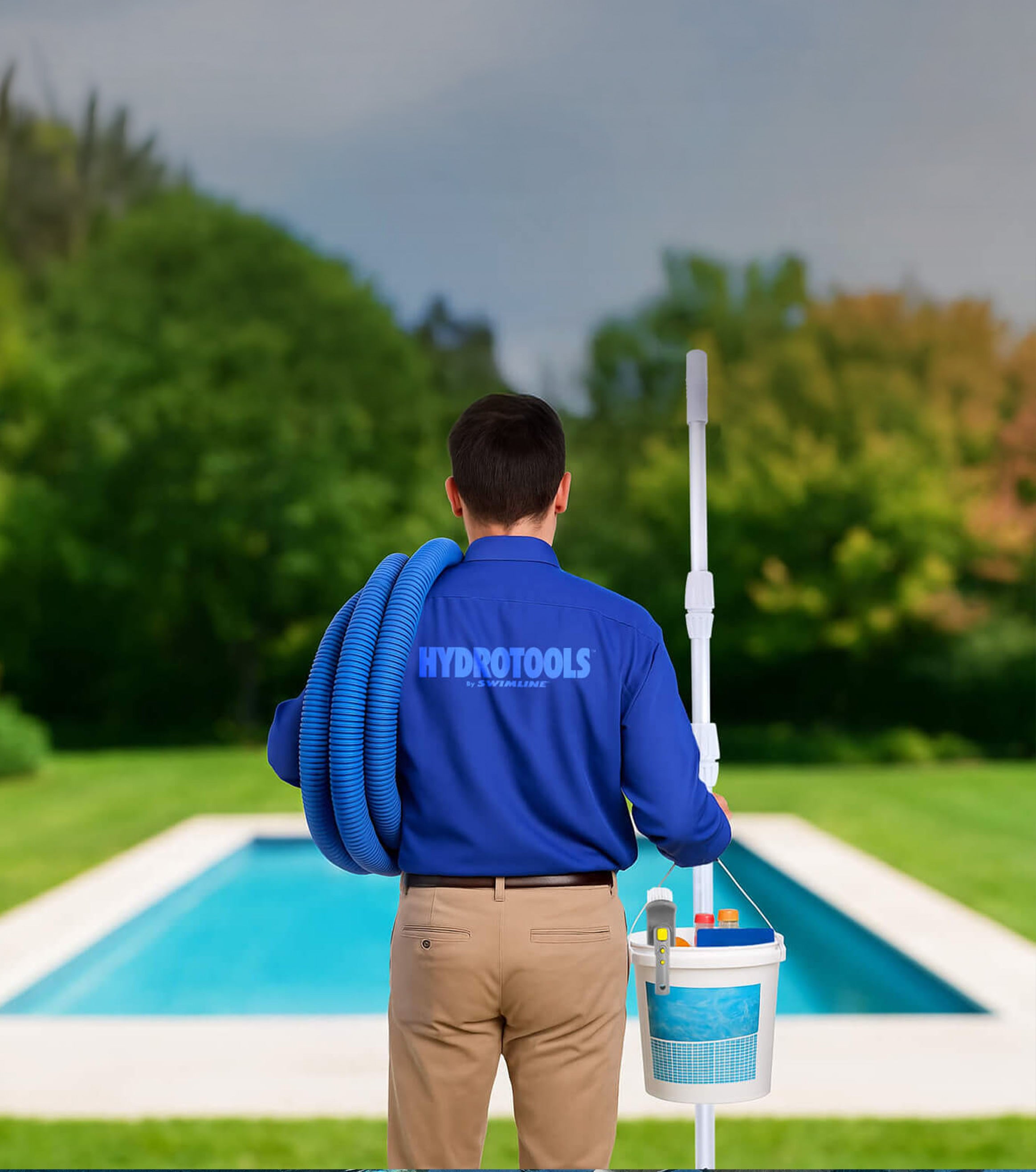Person in a blue 'Hydrotools' shirt holding pool cleaning equipment by a pool.